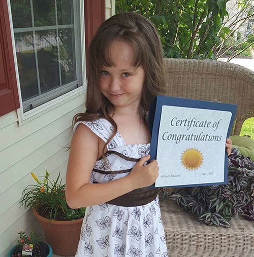 Adopted or fostered child proudly holding certificate of achievement.
